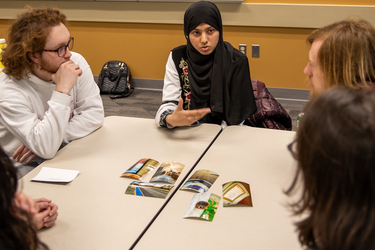 Person speaking to a group with printed photos on table